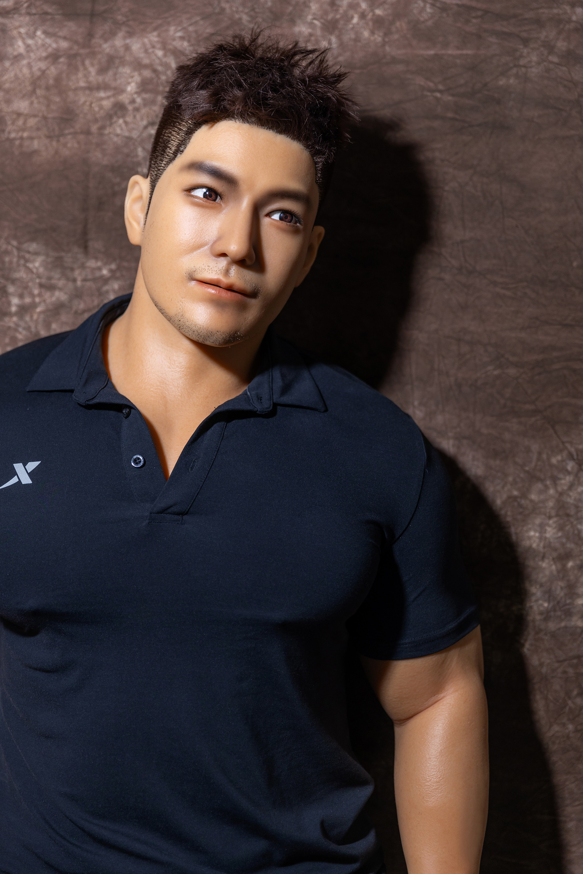 Male sex doll, wearing navy blue polo shirt, muscular physique.