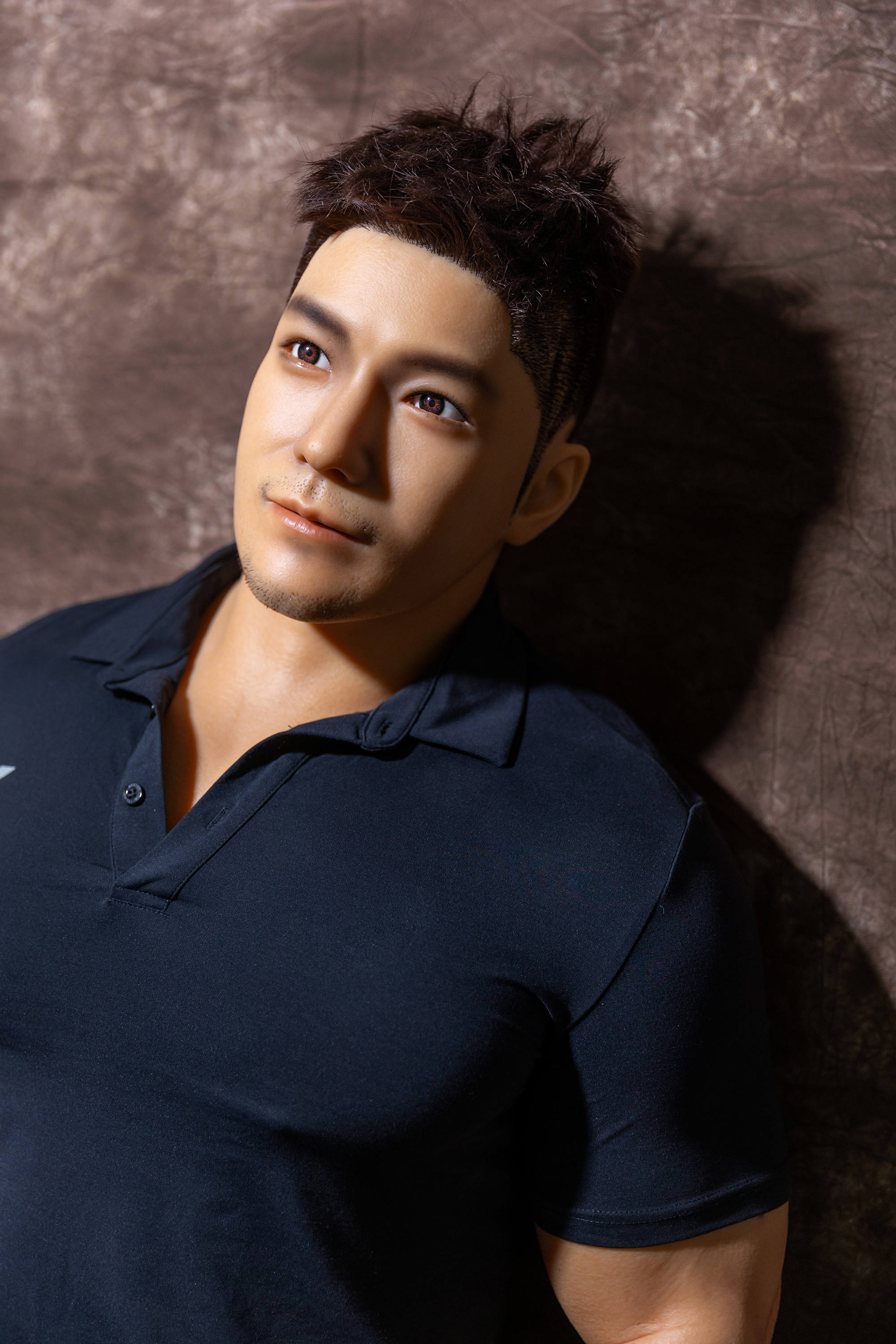 Realistic male sex doll, close-up of face, black shirt, seamless skin.