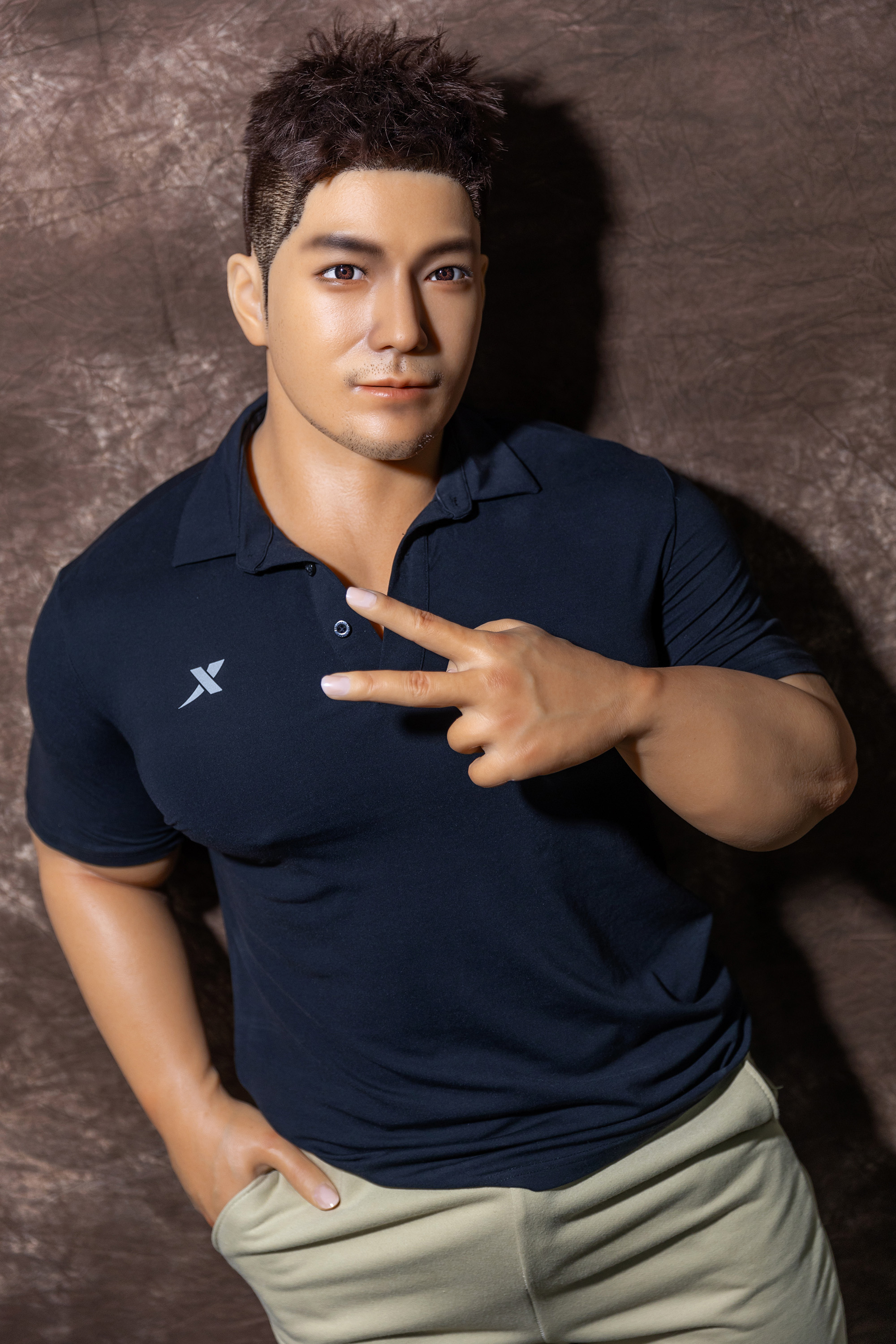Male sex doll in a navy blue polo shirt and beige pants.