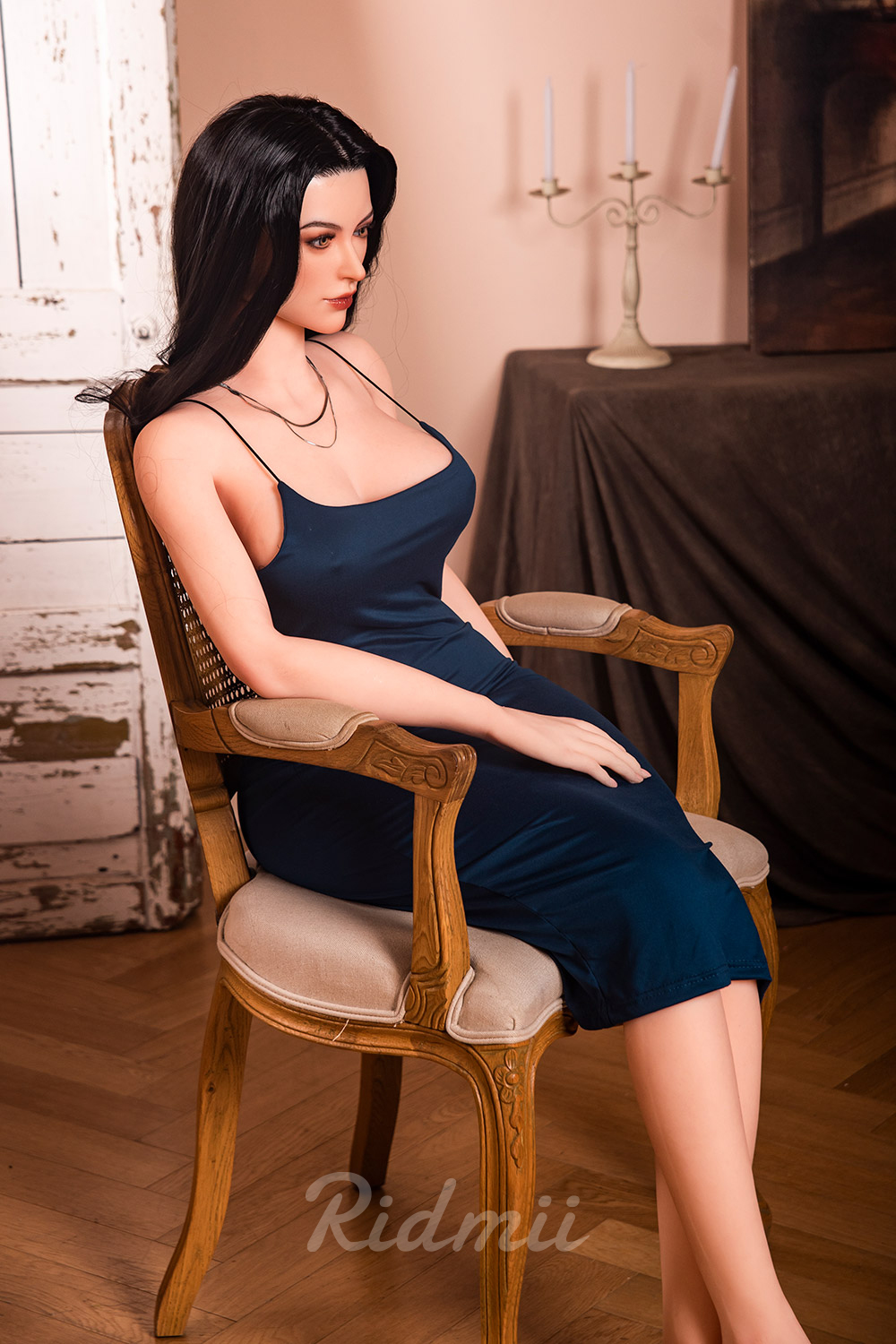 Realistic sex doll in blue dress sitting on a chair