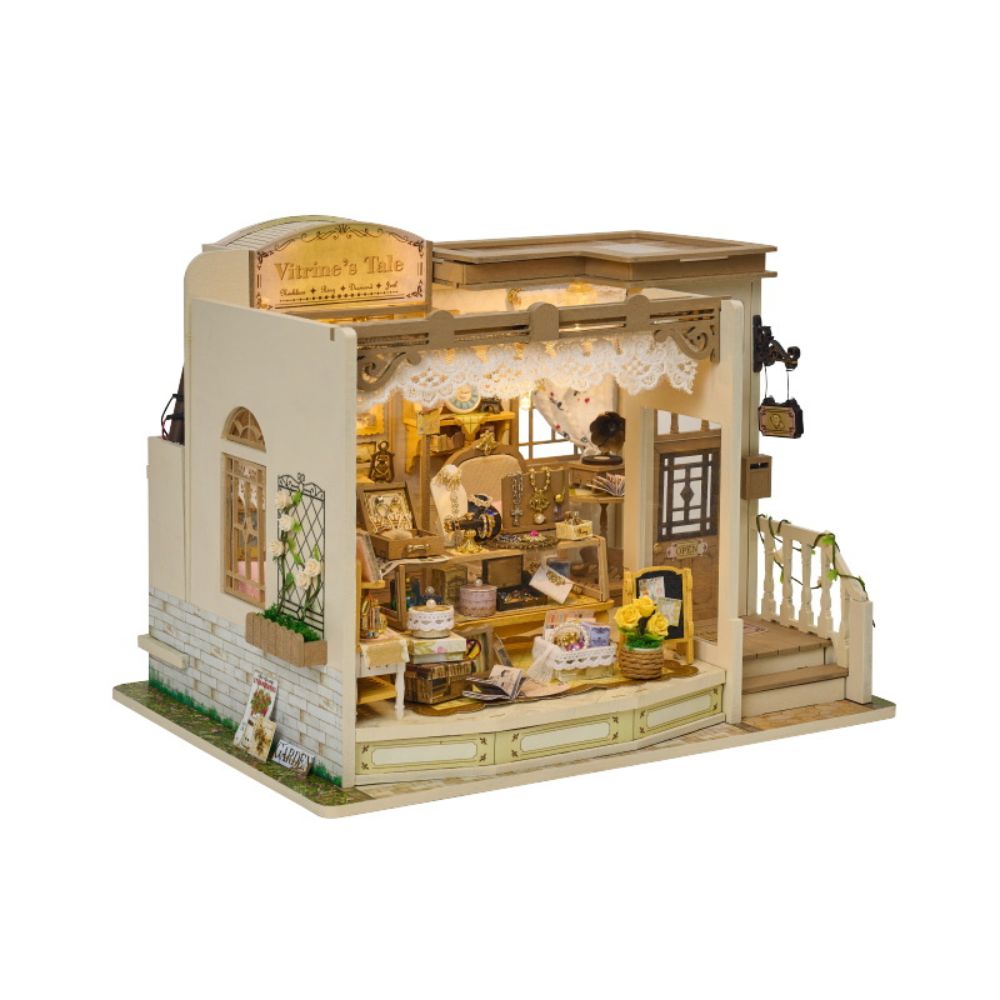 A large bay window showcases a meticulously detailed interior with numerous miniature items, including shelves stocked with jewelry, small decorative bowls, a tiny book, and a small vase of yellow flowers.