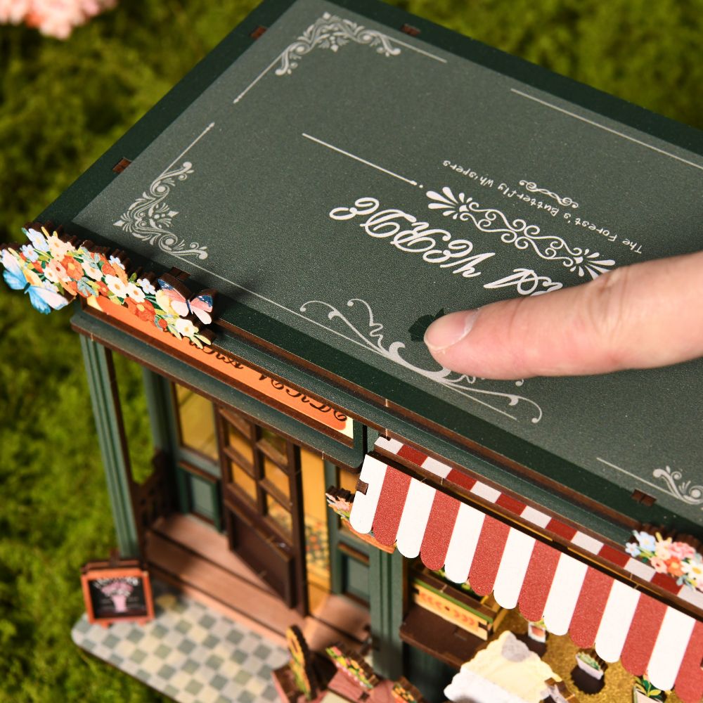  A people can press down on the top panel of the dark green miniature structure, likely to activate the touch-activated LED lights commonly featured in these kits. 