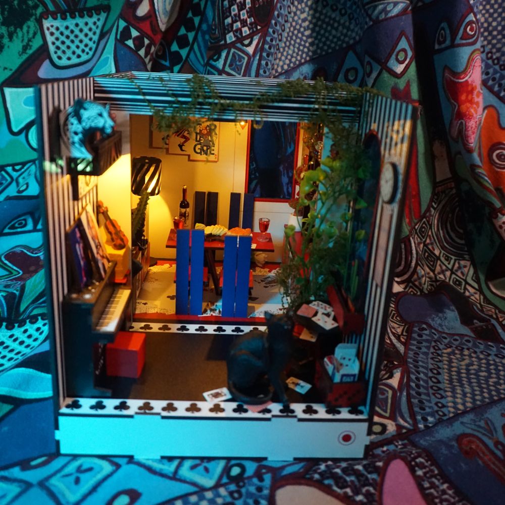 The diorama features a piano, a dining table with two blue chairs, and various decorative elements.
The overall aesthetic is described as bold, joyful, and designed to make people rethink what a space can be.