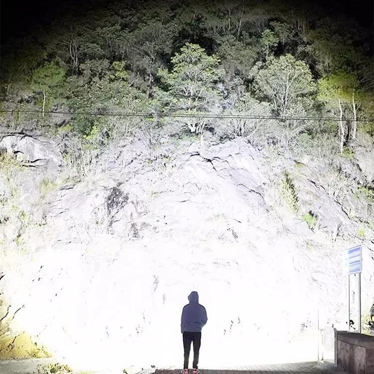Person in hoodie illuminated by powerful auto LED spotlight against rocky hill, night scene