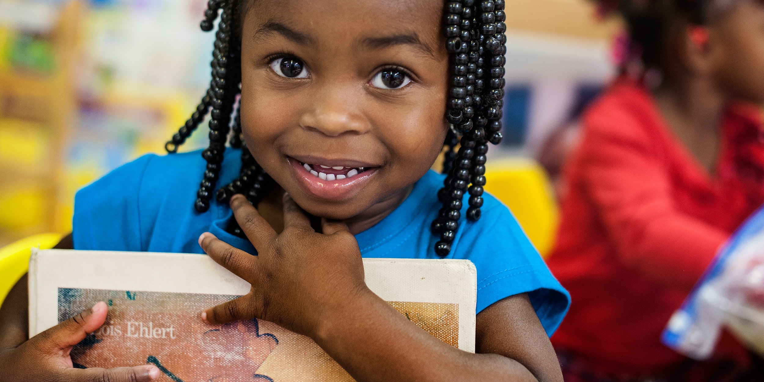 A smiling preschooler holds a book to her chest at the Early Steps to School Success (ESSS) program in Barnwell, South Carolina: Photo credit: Susan Warner/Save the Children, October 2014.