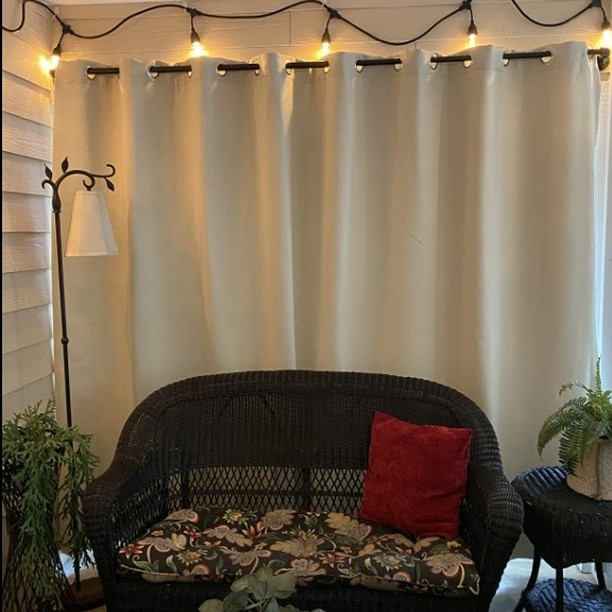 White Outdoor Curtains on a covered patio beside warm string lights and wicker seating
