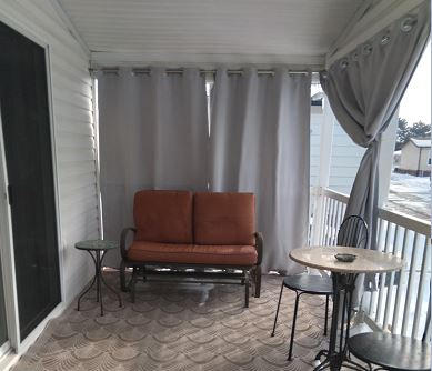 Gray outdoor curtains on a covered porch, ready to be drawn for privacy and light weather screening