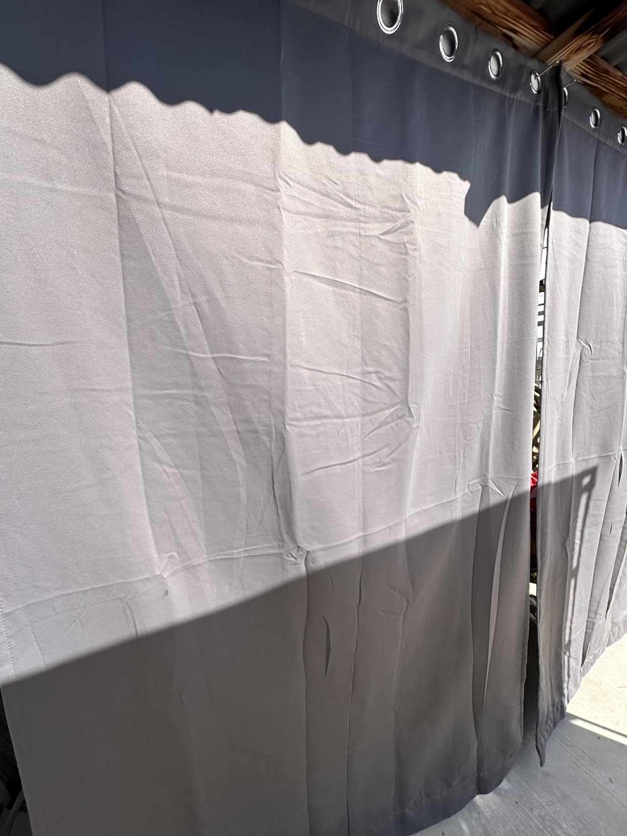 Dark outdoor curtain panels with metal grommets installed beneath a wooden beam