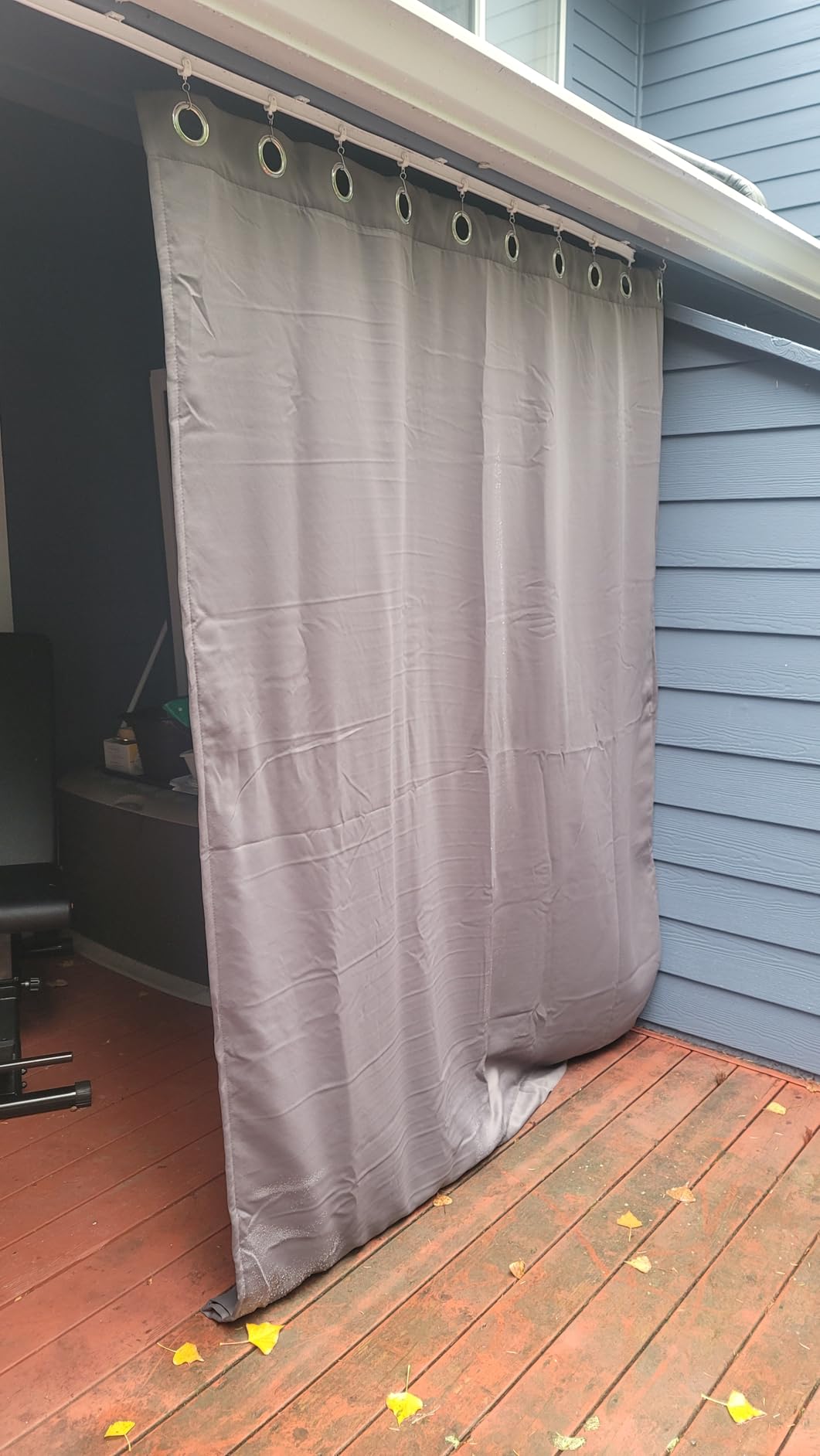 Gray outdoor curtain panel with metal grommets installed across a covered gazebo-style deck opening