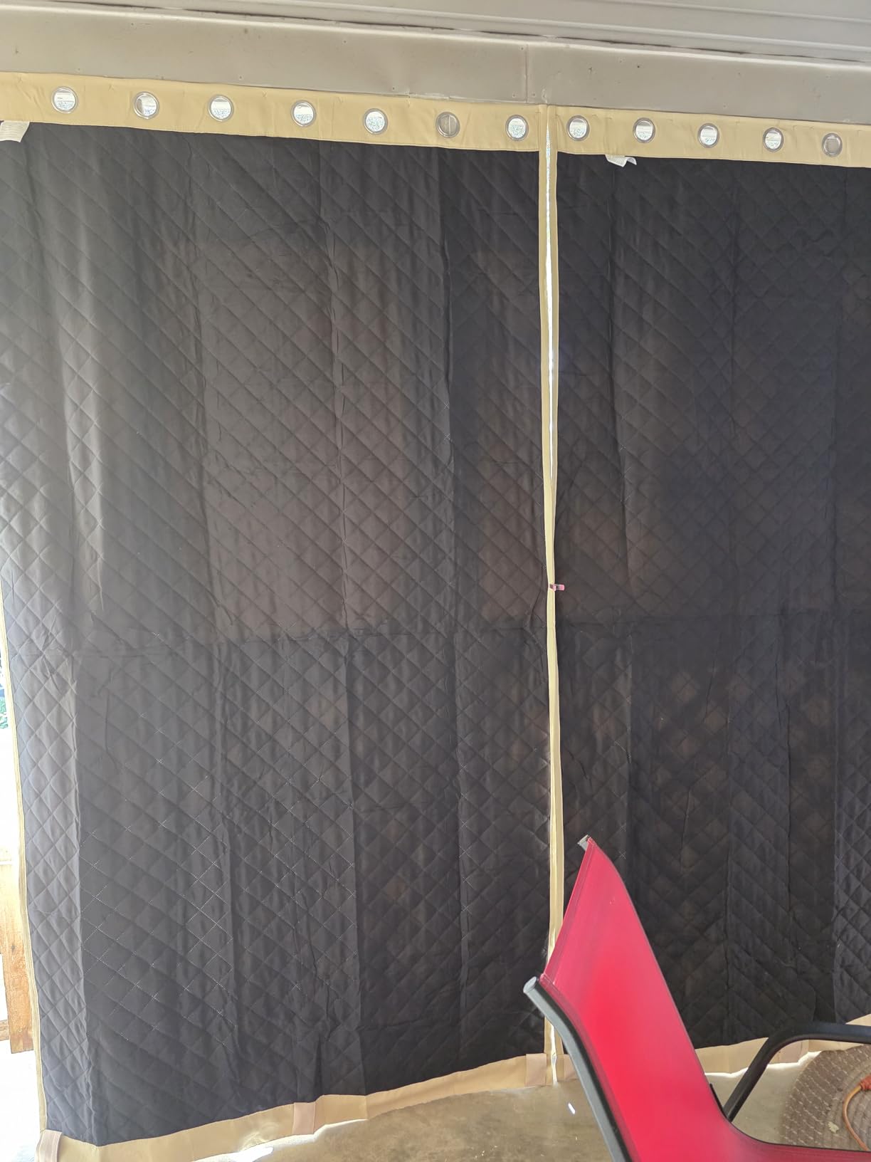 Black quilted outdoor winter curtain panels with grommets installed across a covered patio opening