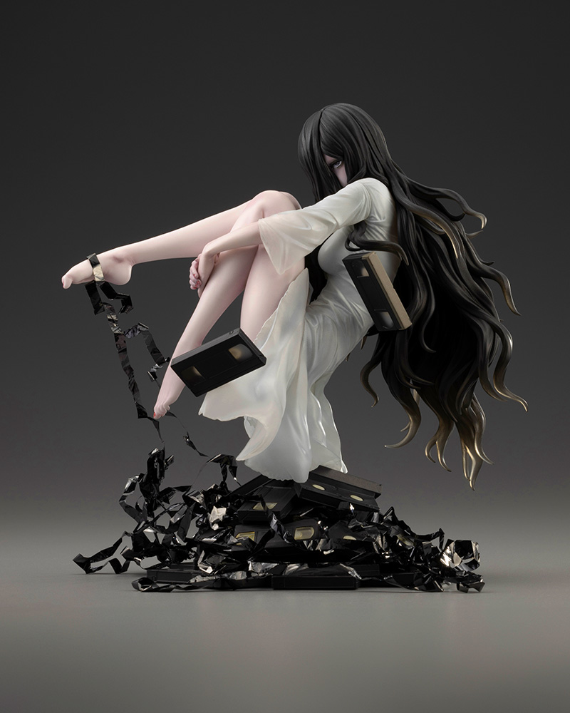 Side view of the Sadako figure hugging her knees as she hovers above a mound of videotapes with loose tape trailing from her hand