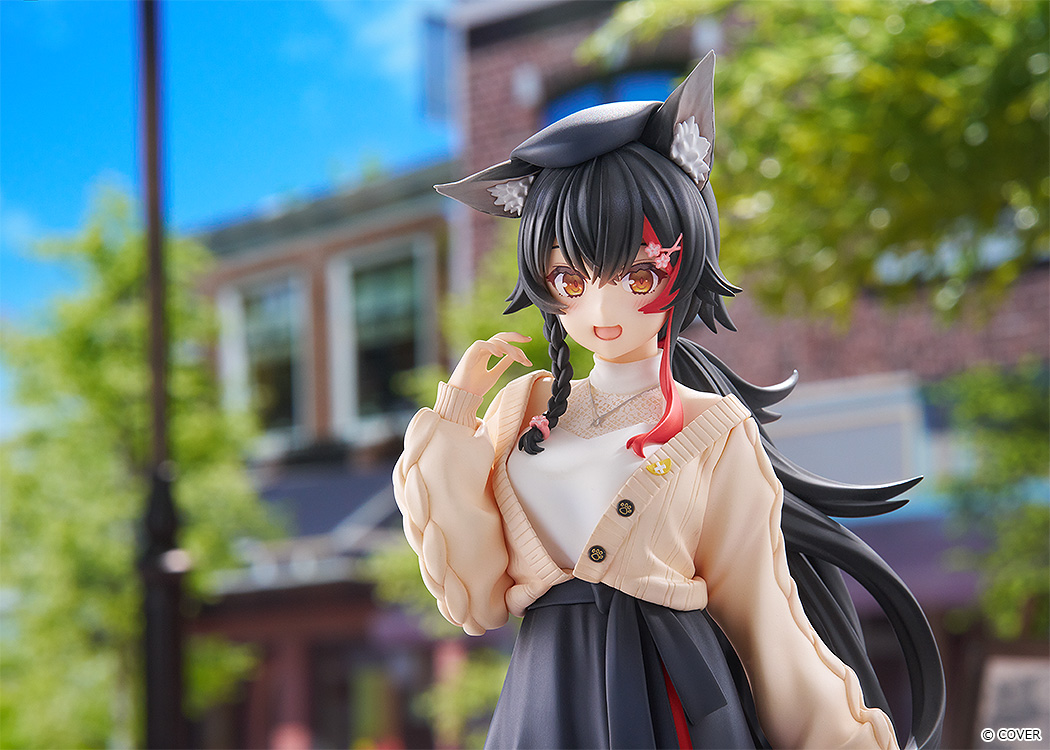 Upper-body shot of the Mio figure on a sunny town street, smiling with one hand raised, her cream cardigan and black hair lit by the sun