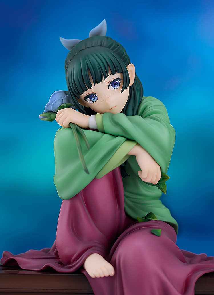 Close-up of the Maomao figure resting her chin on her folded arms, with freckles, blue-violet eyes, dark green hair tied with a pale blue ribbon and a blue rose in one hand