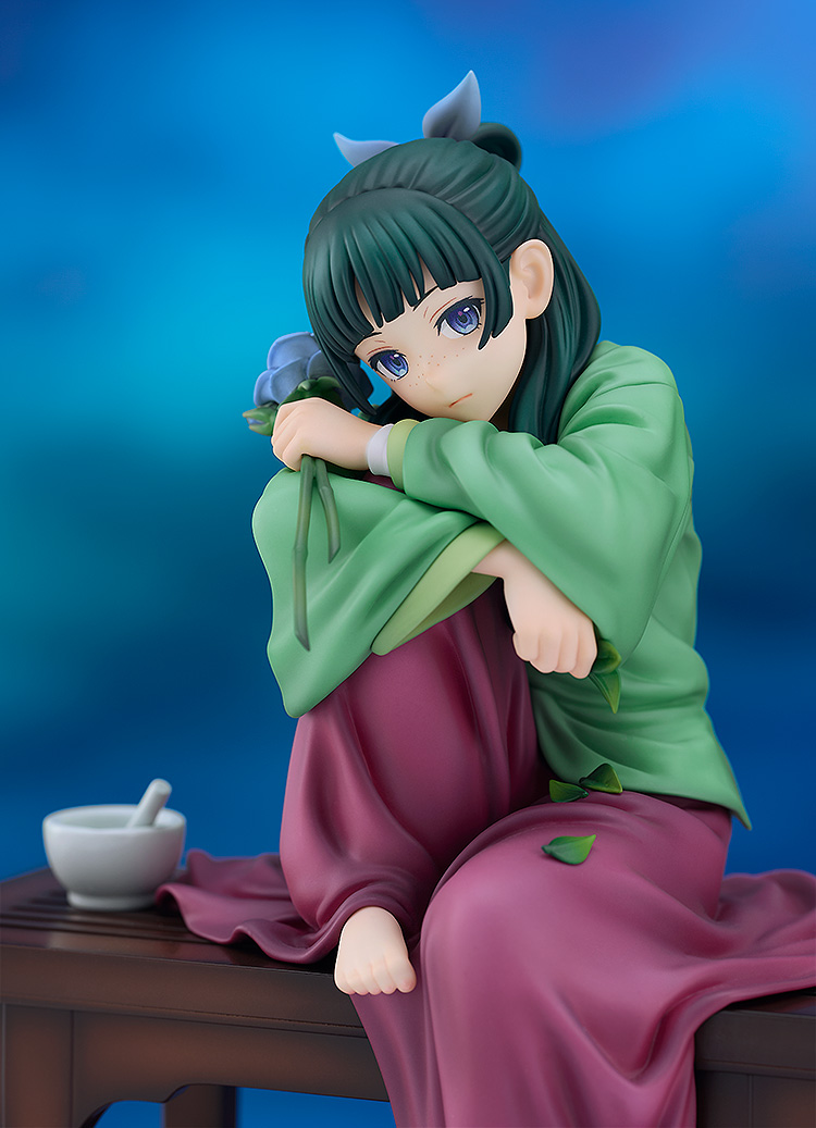 Side view of the Maomao figure against a blue backdrop, hugging her knees on the bench with a white mortar and pestle next to her