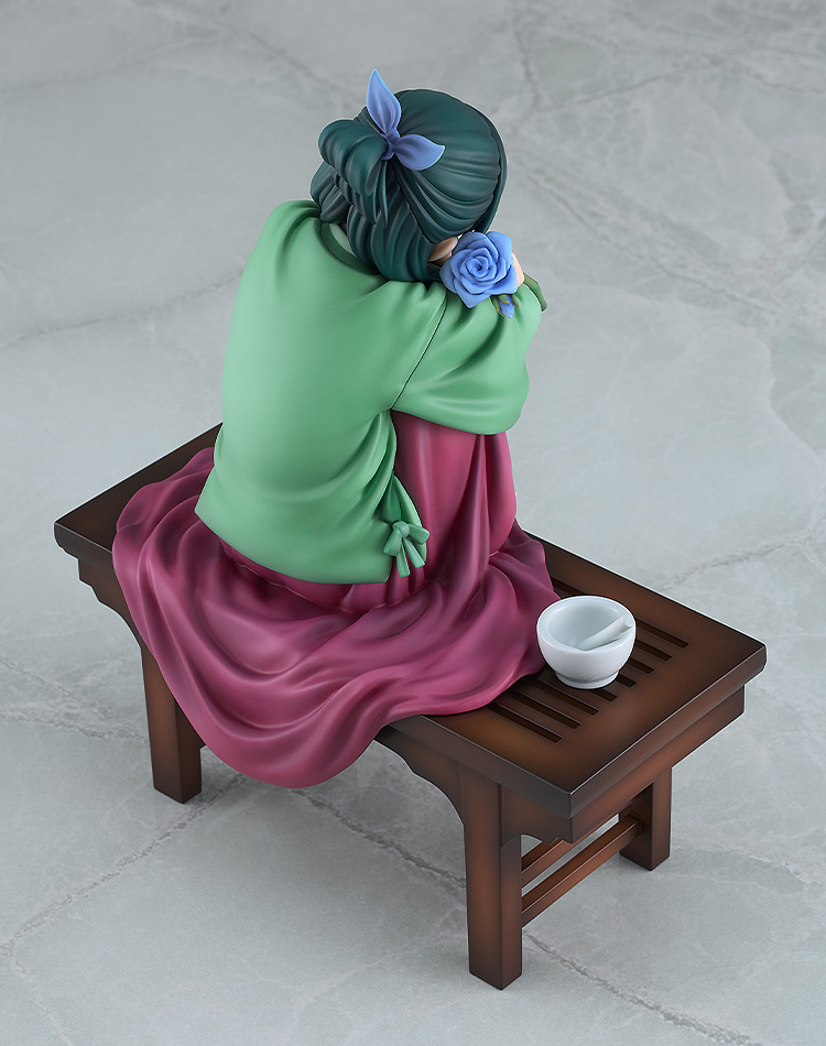 View of the Maomao figure from behind and above, showing her tied-up green hair with a blue ribbon, a blue rose at her shoulder and the mortar on the slatted bench