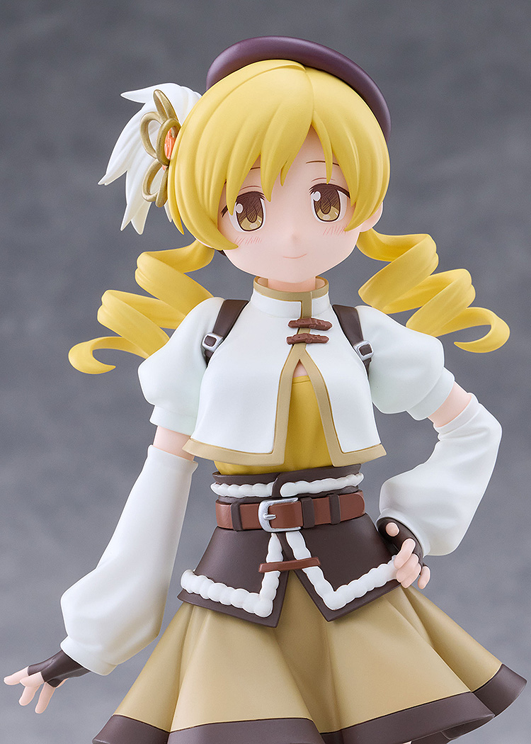 Close-up of the Tomoe Mami figure smiling, with golden drill-curl twin tails, a brown beret with a flower ornament and a white puffed-sleeve jacket