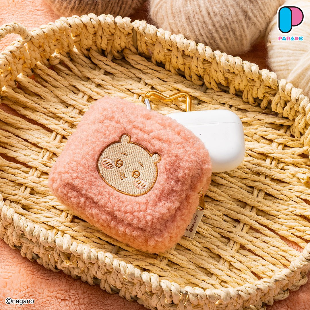 Pink fluffy Chiikawa face pouch with a gold carabiner in a woven basket next to a white wireless earbud case