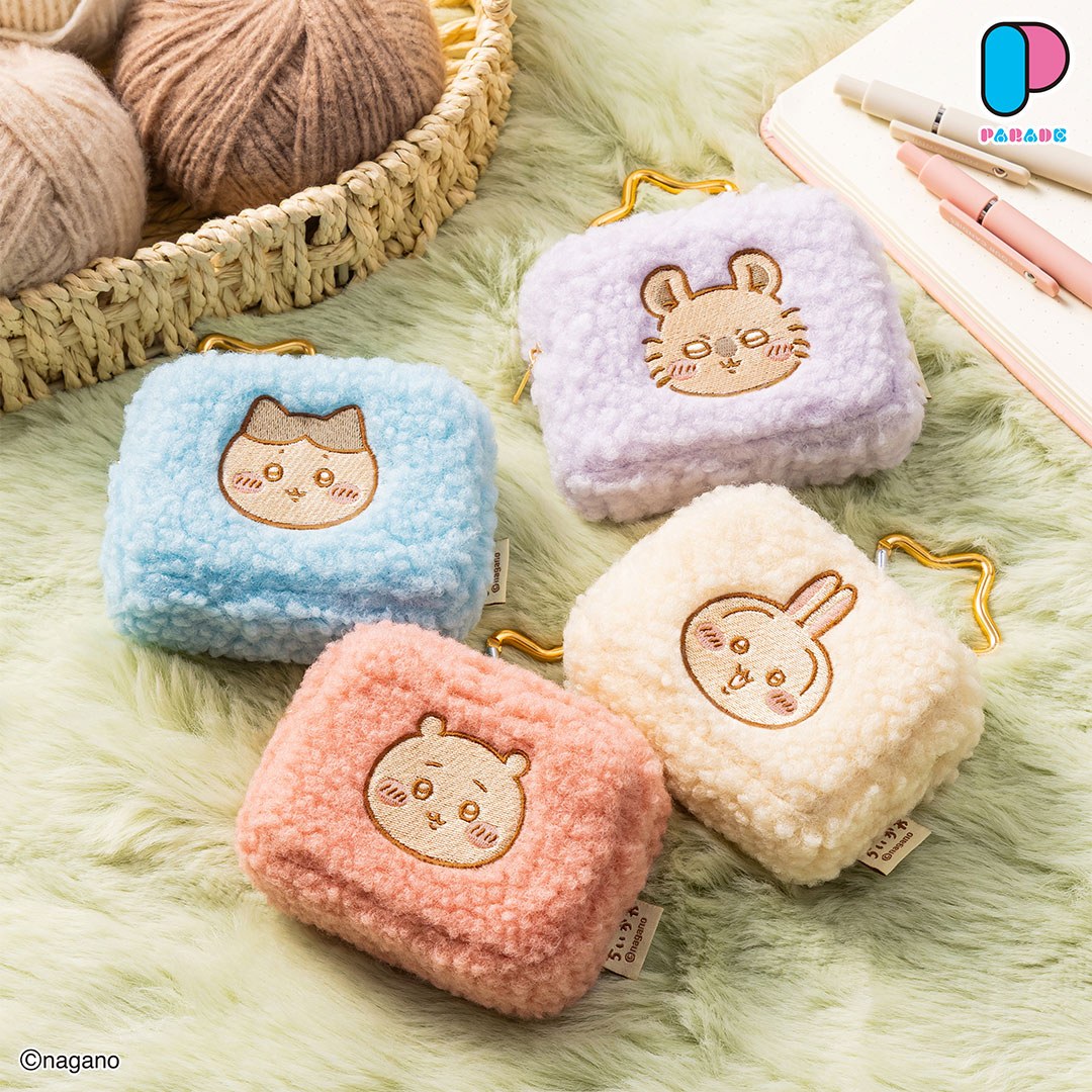 Four Chiikawa fluffy pouches in pink, blue, cream and lilac with embroidered faces on a sage-green fluffy rug