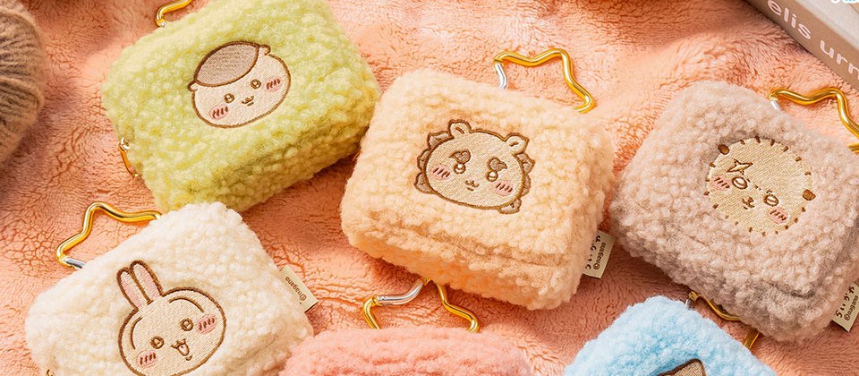 Close-up of three Chiikawa fluffy pouches in sage green, apricot and beige showing the embroidered faces and gold carabiners