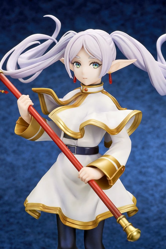 Upper-body view of the Frieren figure against a deep blue backdrop, gripping her red staff with both hands, showing the gold-trimmed capelet and black belt