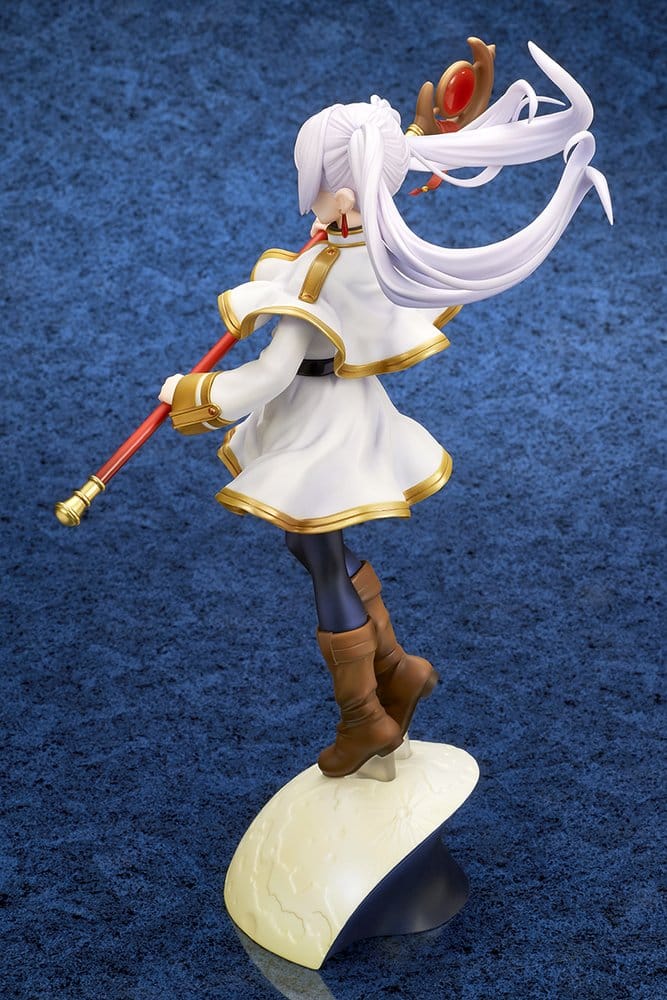 Rear three-quarter view of the Frieren figure on the moon base, her staff stretched out to one side and her hair and cape streaming in the wind against a blue backdrop