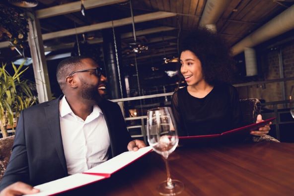 Ebony man and woman at a bar, laughing and holding menus.