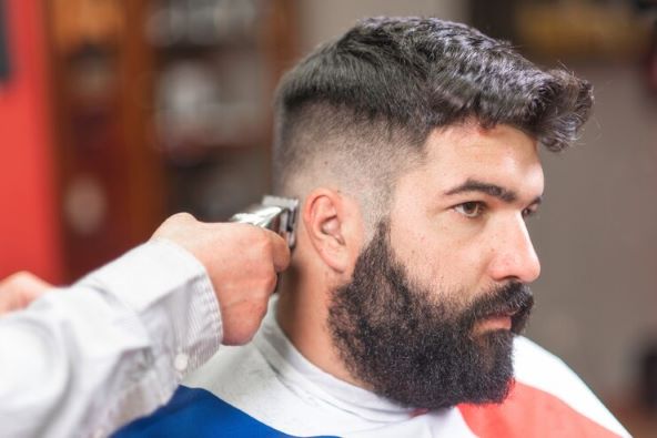 handsome bearded man getting haircut by barber