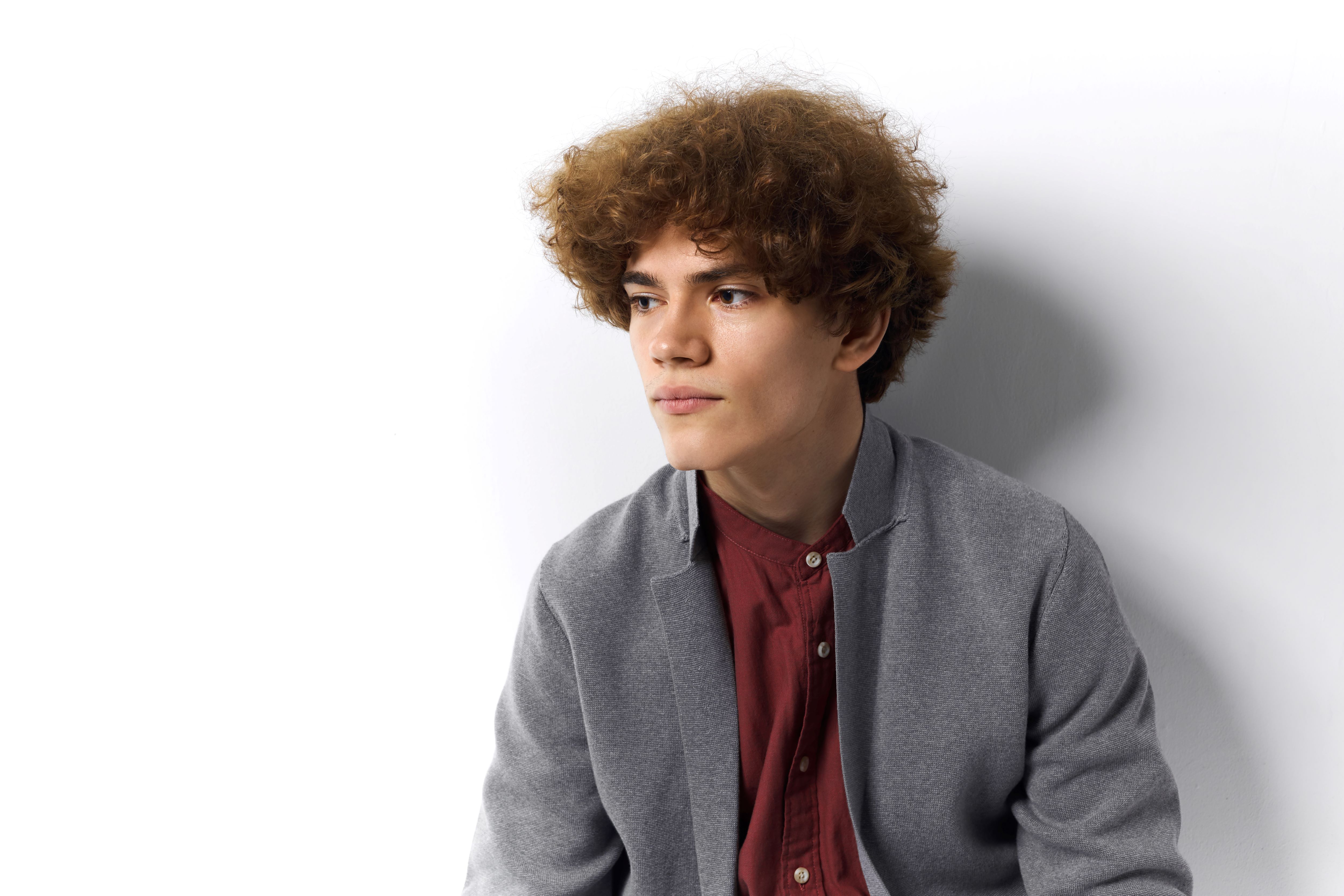 Young model with short curly hairs dressed in red shirt and a blue jacket