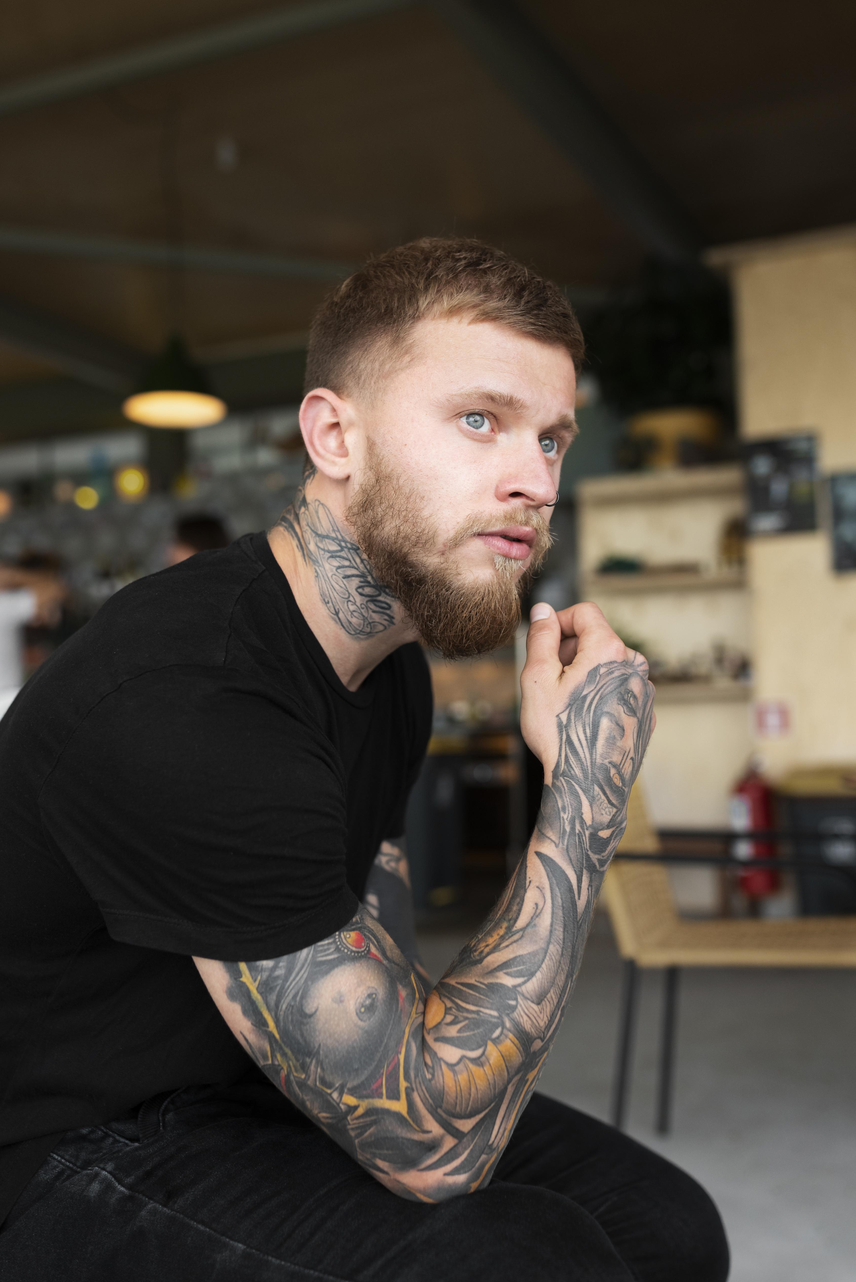 Tattooed bearded man in black outfit showing the Crew Cut hairstyle