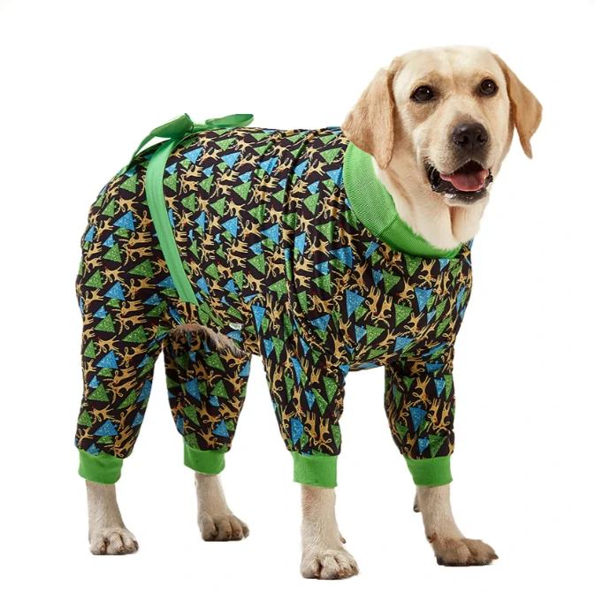 Labrador in black holiday pajamas with golden reindeer and green Christmas trees, featuring a green collar and decorative green bow.