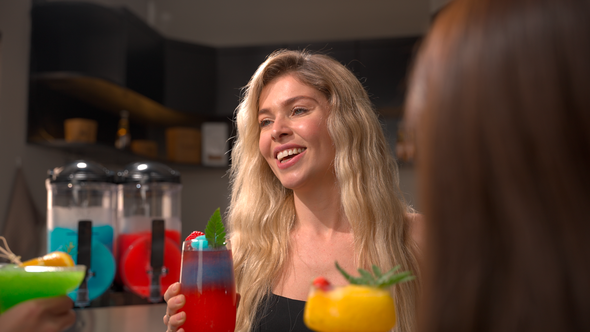 Smiling woman holding a colorful red and blue slushy drink with friends, with commercial slushy machines in the background, illustrating customer experience in a U.S. slushy bar.