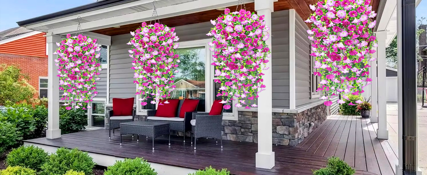 Au&szlig;enterrasse mit grauen Korbm&ouml;beln und roten Kissen. Vier H&auml;ngek&ouml;rbe mit leuchtend rosa und wei&szlig;en Blumen zieren die Vorderseite. Stein- und Holzelemente sorgen f&uuml;r eine gem&uuml;tliche Atmosph&auml;re