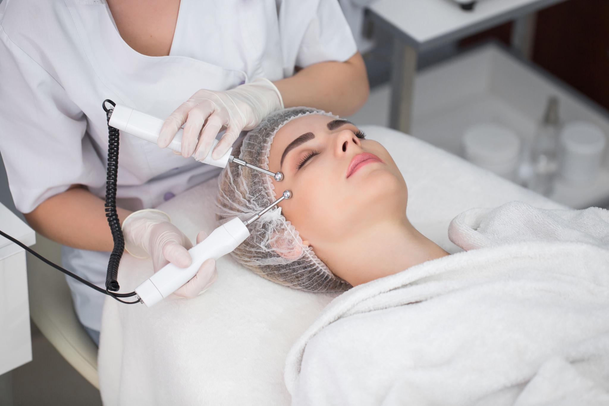 Macro close up portrait of woman having cosmetic galvanic beauty treatment in spa.Therapist applying low frequency current with electrodes on face.