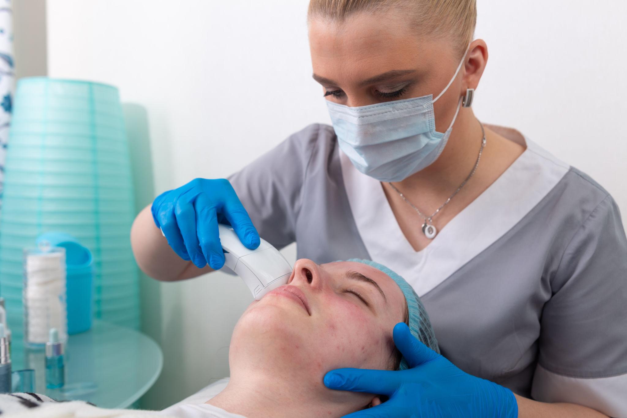 Young woman receiving electric galvanic anti-aging face spa massage at beauty salon.