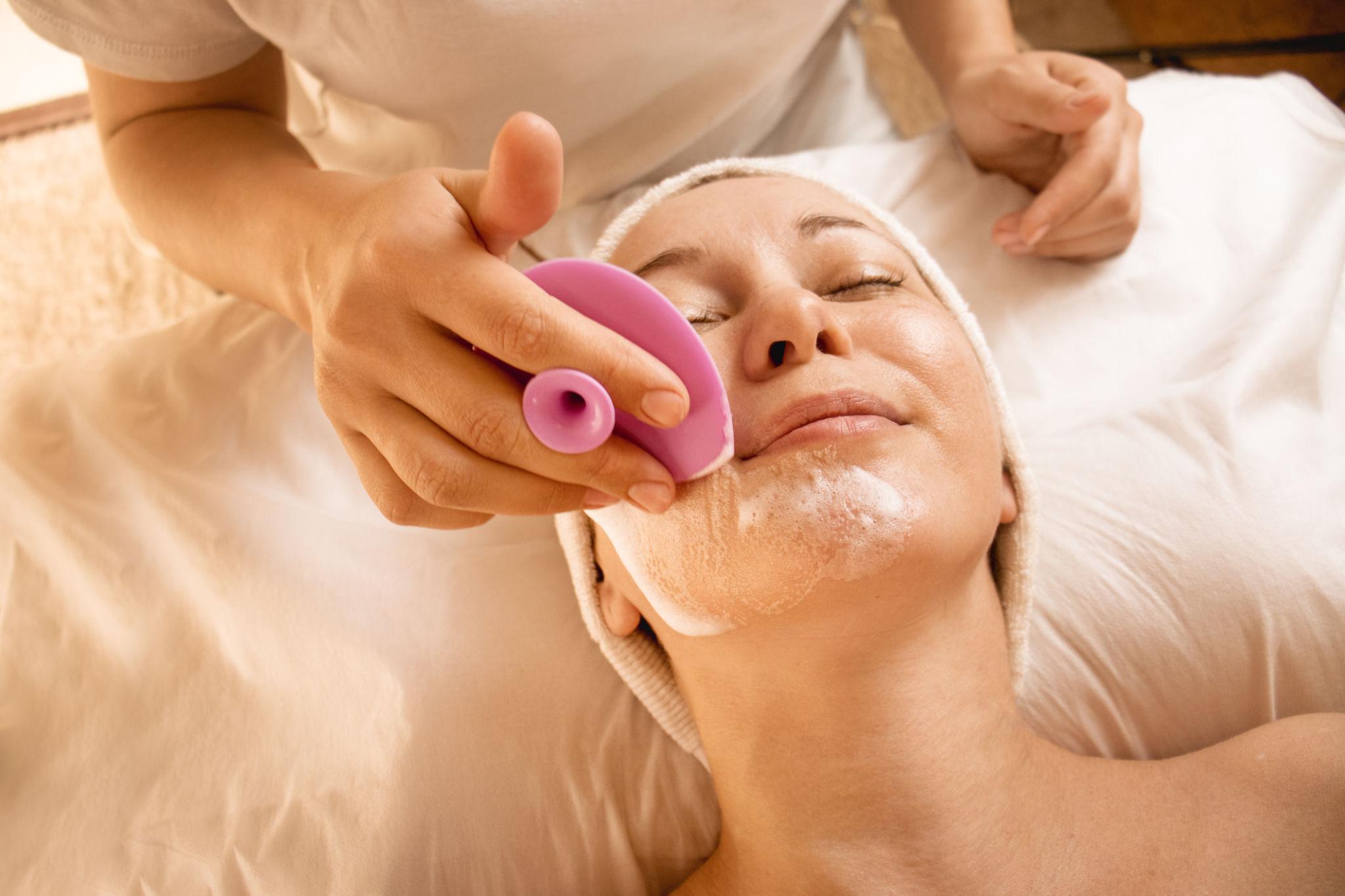 cleansing the skin with a silicone brush, cosmetologist cleanses the client's skin close-up,pink cosmetic silicone brush