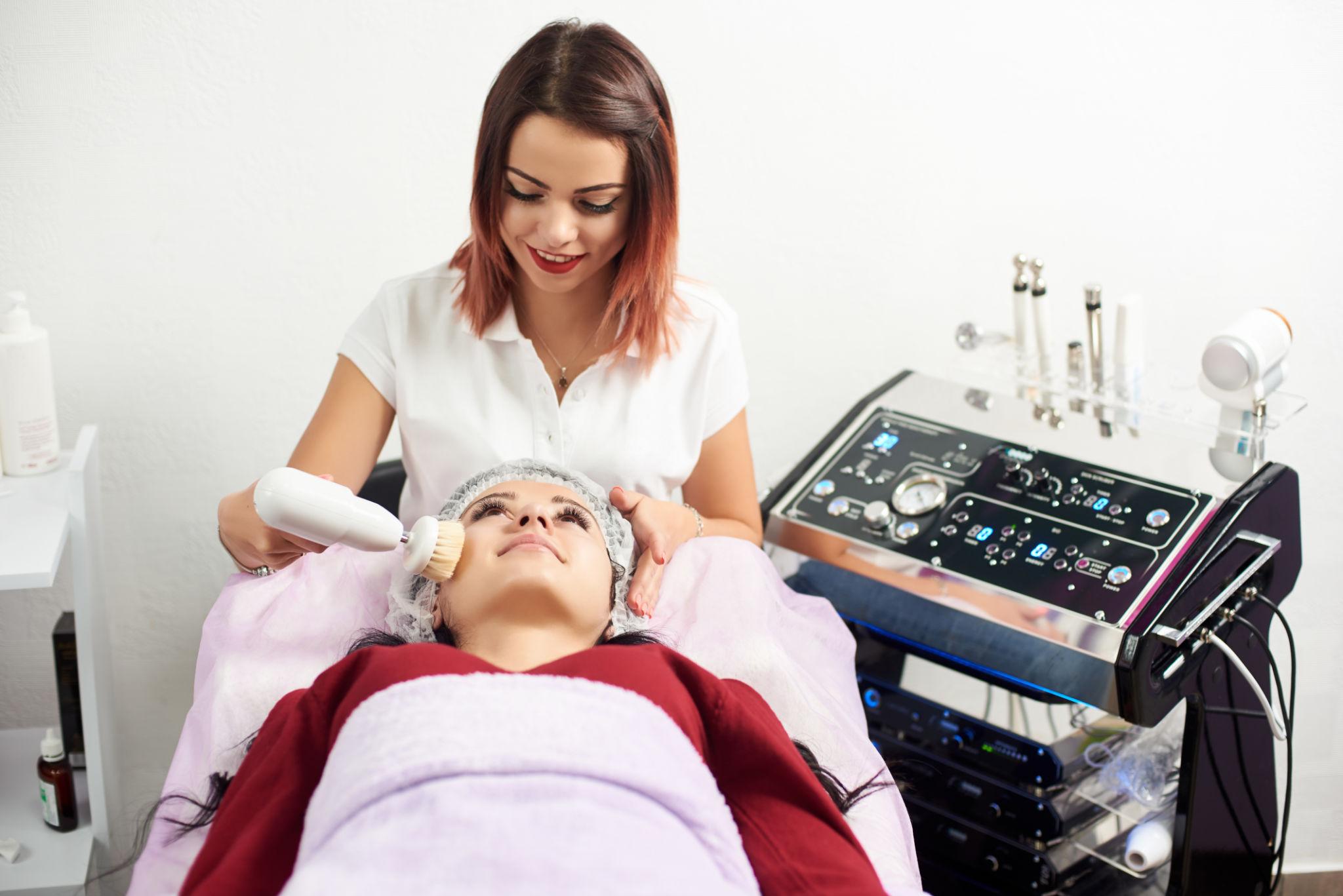 Cosmetologist makes the apparatus a procedure of Hardware face cleaning with a soft rotating brush of a beautiful, young woman in a beauty salon.