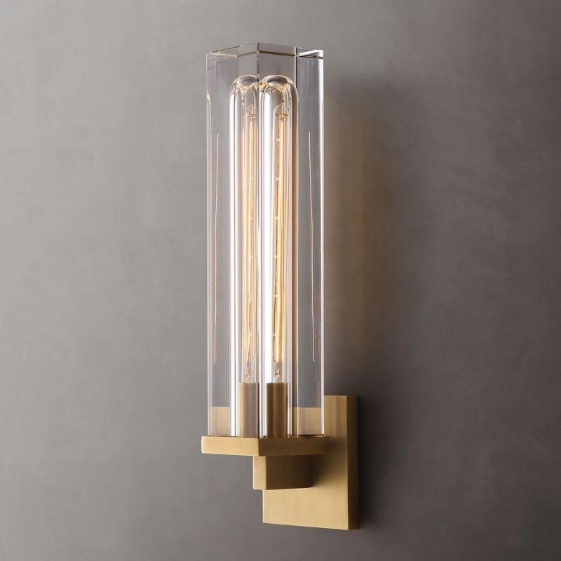 The Zylero Savill Wall Lamp in gold offers a captivating blend of solid crystal and void, with a brass frame that enhances the Edison bulb's warm glow.