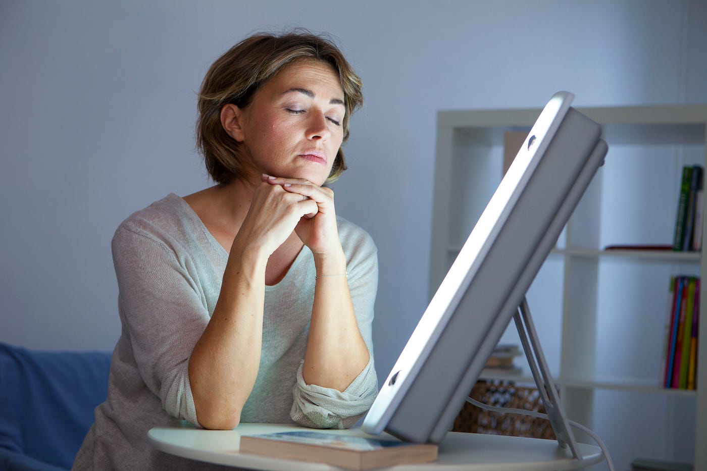 Do SAD Lights Really Work?-StressNoMore. Woman using a bright light therapy lamp indoors, illustrating treatment for seasonal affective disorder (SAD) and low mood during darker months.