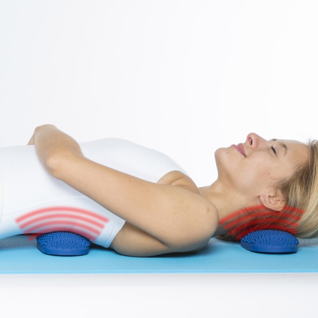 Dr Cohen’s Heatable AcuPads in use, person lying on a yoga mat with blue textured heat therapy pads positioned under the back and neck.