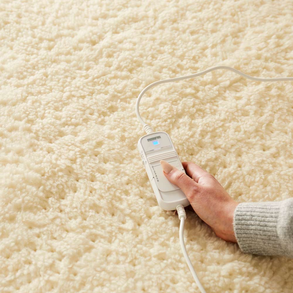 Hand adjusting Beurer heated mattress cover controller on soft teddy fleece electric bed warmer.