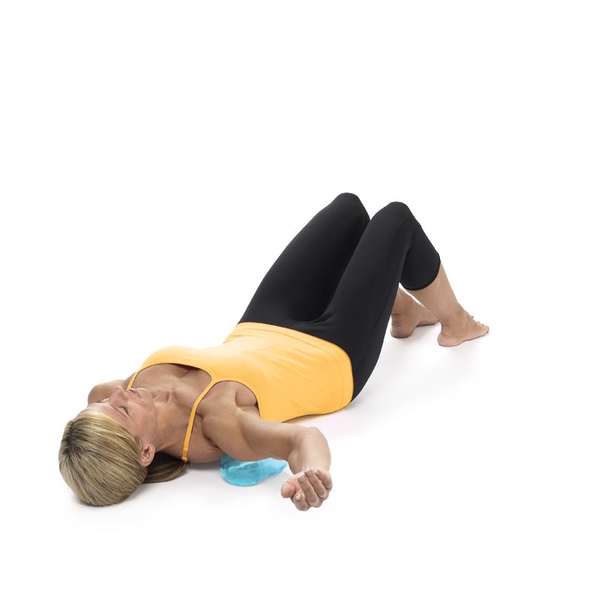 Woman lying on her back using a Franklin Mini Roller under the upper spine and shoulder area, demonstrating a gentle relaxation and mobility exercise to release tension, support spinal alignment, and improve body awareness during floor-based stretching.