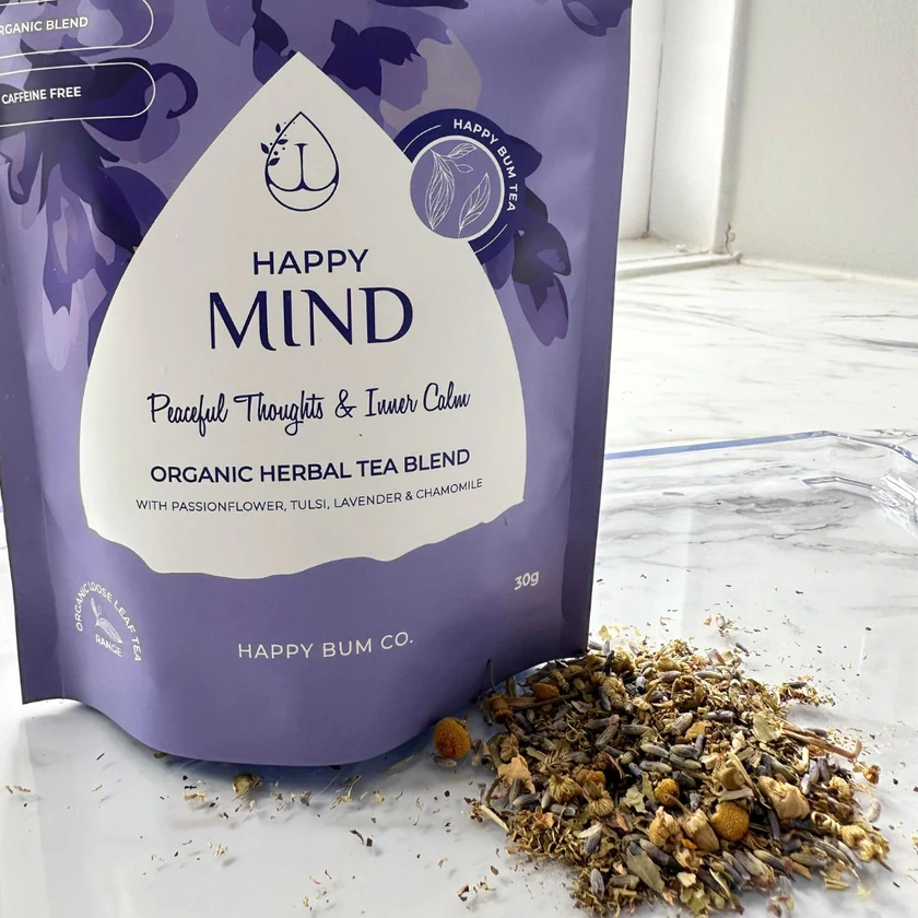 Happy Bum Co Happy Mind organic herbal tea blend packaging with loose leaf herbs beside the pouch, featuring passionflower, tulsi, lavender and chamomile. A caffeine-free calming blend for relaxation, suitable for belly tea or enema preparation.