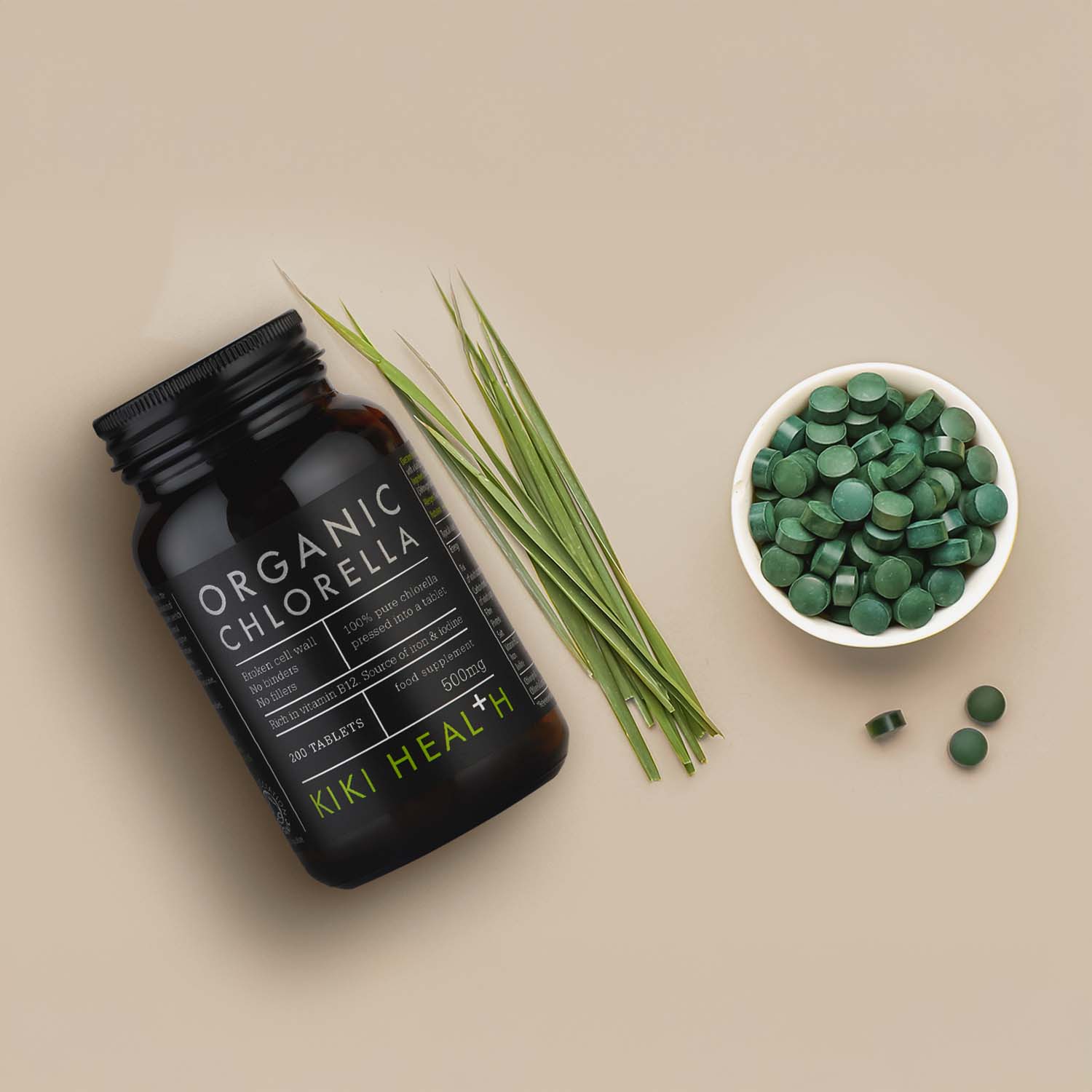 KIKI Health Organic Chlorella Tablets shown in a dark glass jar alongside green chlorella tablets in a bowl and fresh green leaves on a neutral background.