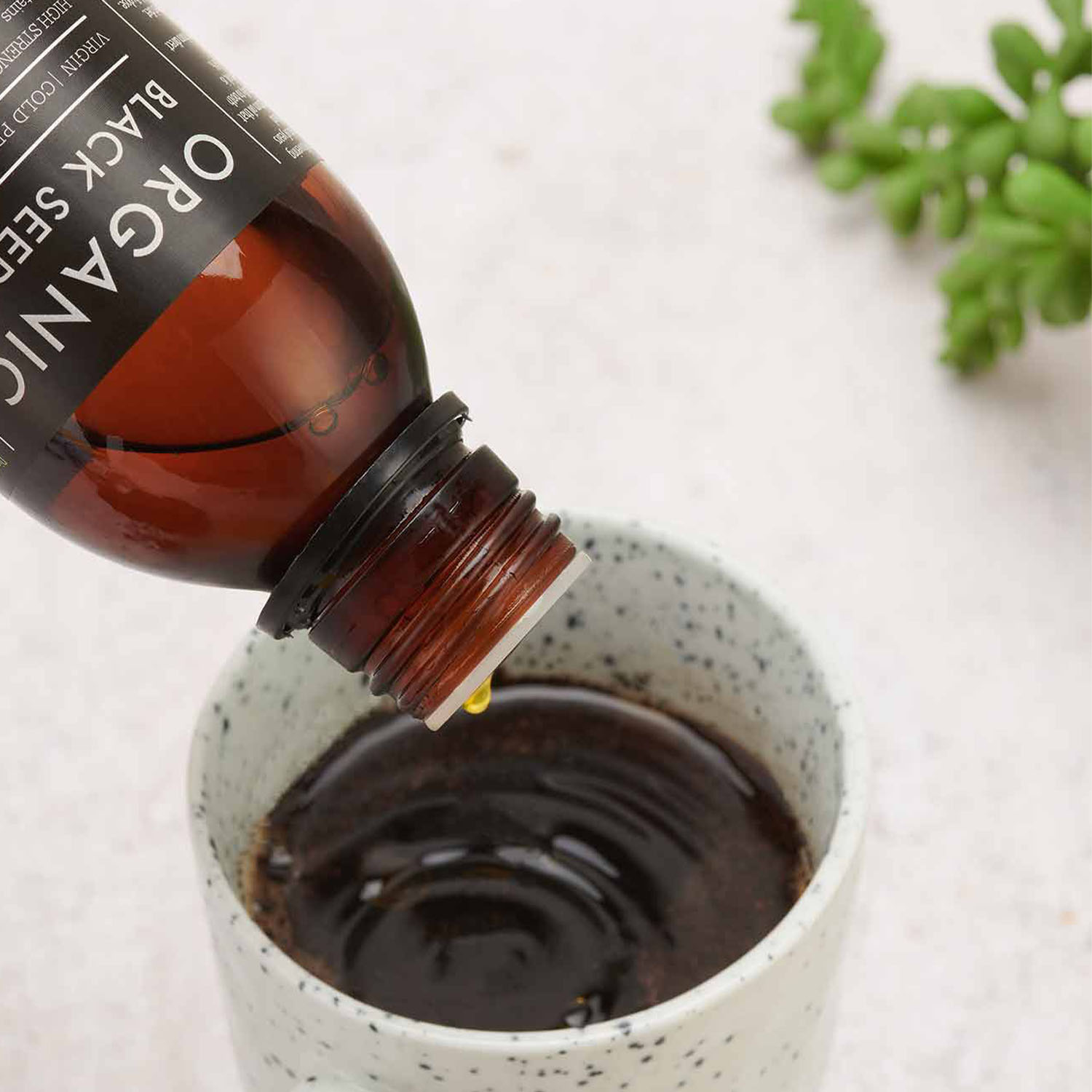 KIKI Health Organic Black Seed Oil bottle tilted as oil is poured into a small ceramic cup in a clean studio setting.