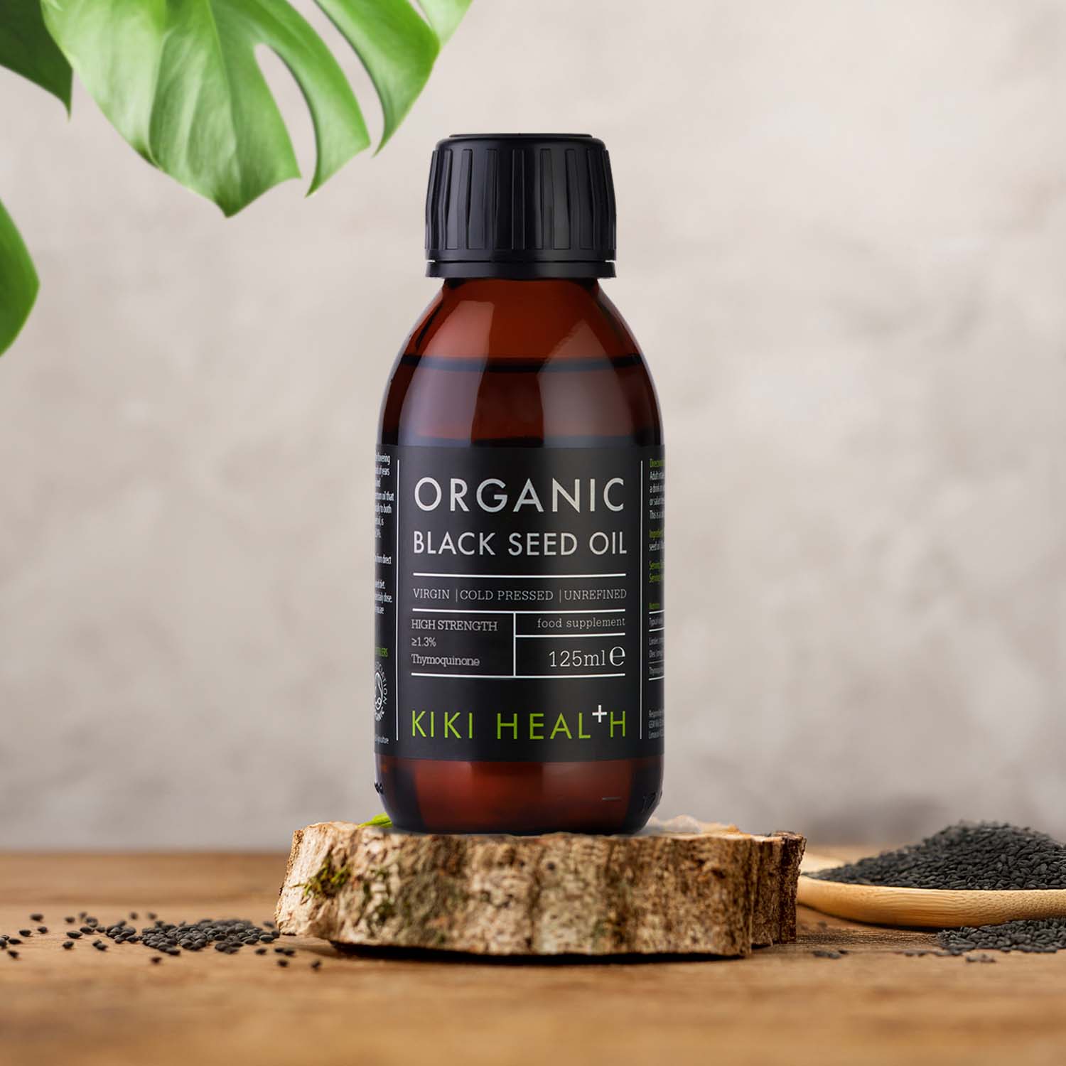 KIKI Health Organic Black Seed Oil in a brown glass bottle displayed on a wooden surface with black seeds and natural decor in a studio setting.