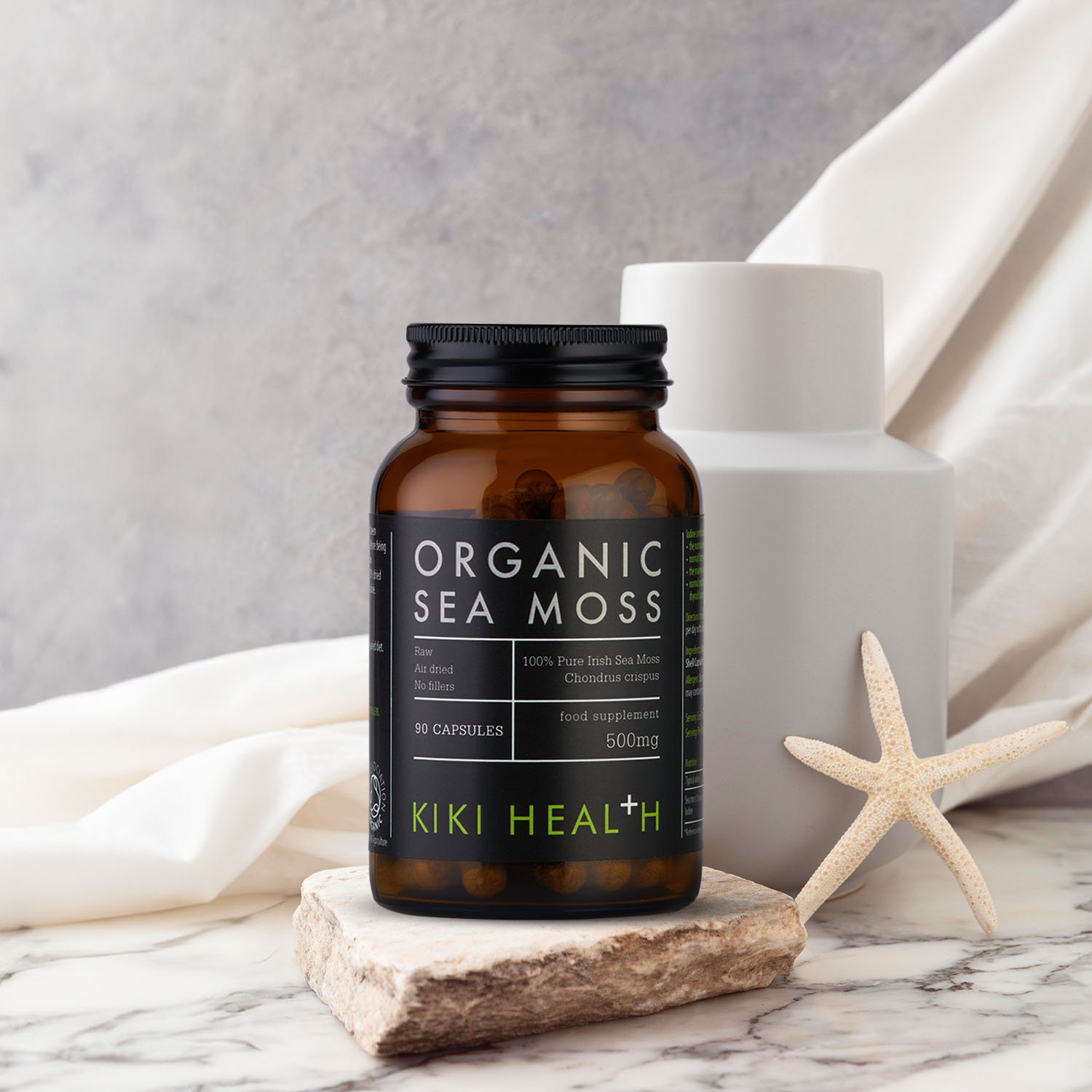 KIKI Health Organic Sea Moss capsules in a brown glass supplement jar displayed on a stone surface with neutral decor in a clean studio setting.