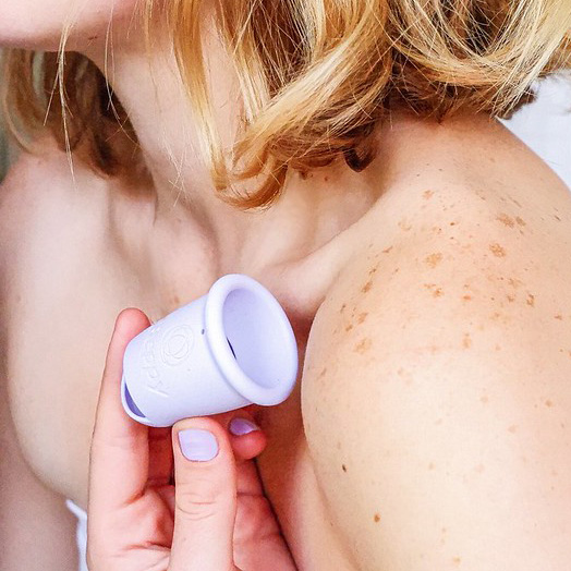 Person holding a Beppy reusable menstrual cup against their shoulder, showing the cup’s flexible shape and smooth silicone design in a lifestyle setting.