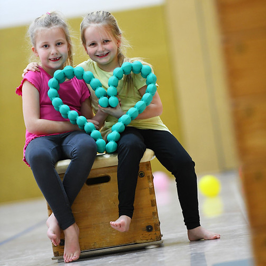 Two children sitting on a gym box holding a Spinefitter junior posture trainer shaped into a heart.