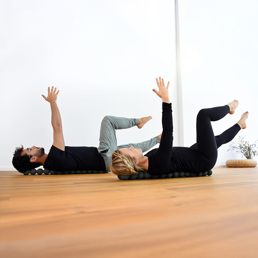 Man and woman performing spinal mobility exercises on the Spinefitter by Sissel, lying on their backs with arms raised to improve posture, core strength, and back flexibility.
