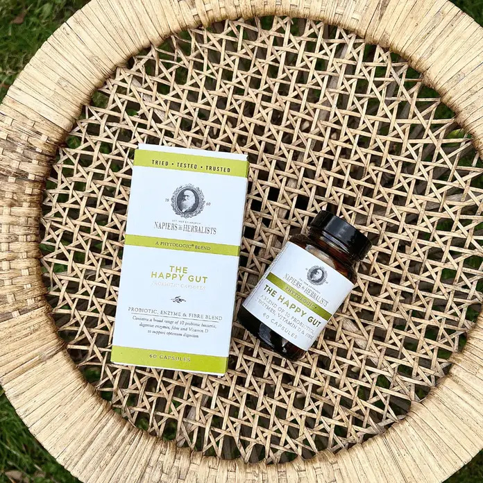 Napiers Phytologic Happy Gut Capsules displayed with bottle and box on a woven tray, showcasing a probiotic, enzyme and fibre supplement formulated with 10 friendly bacteria strains and vitamin D to support digestion and gut health.